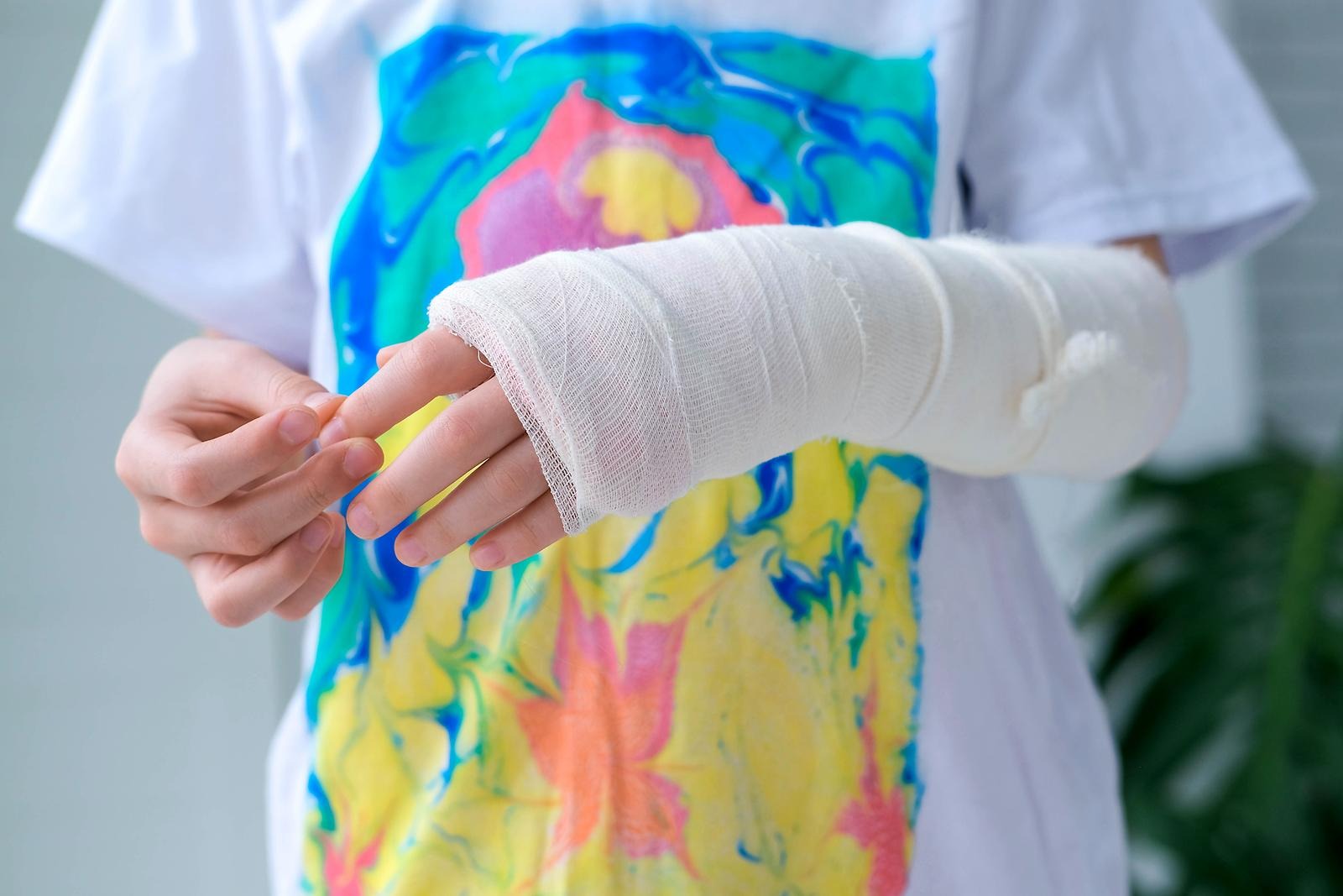 Ett barn ifärgglad t-shirt håller upp en bruten arm i gips. 