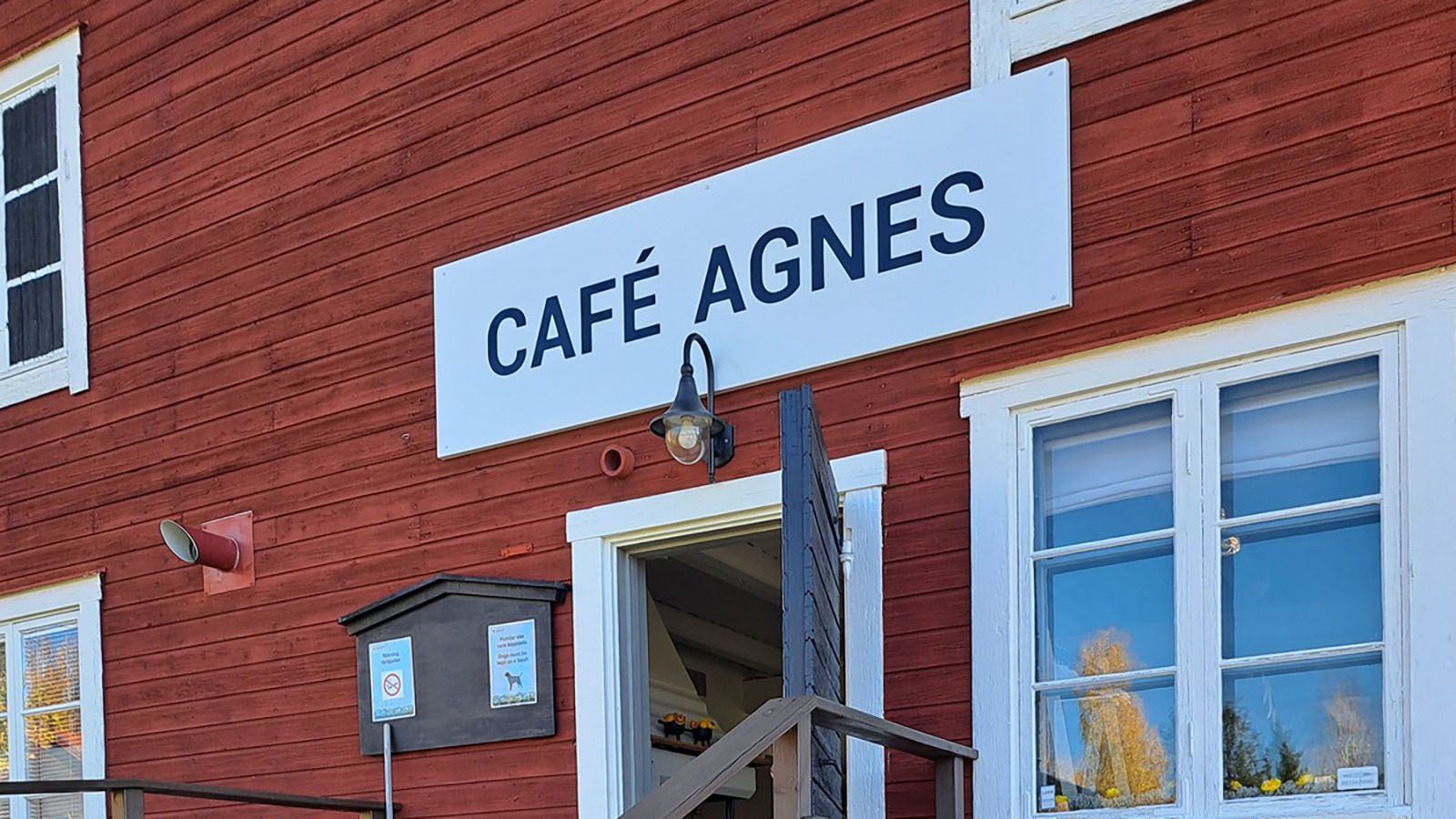 Texten "Café Agnes" på en skylt på en röd husvägg ovanför en dörr.