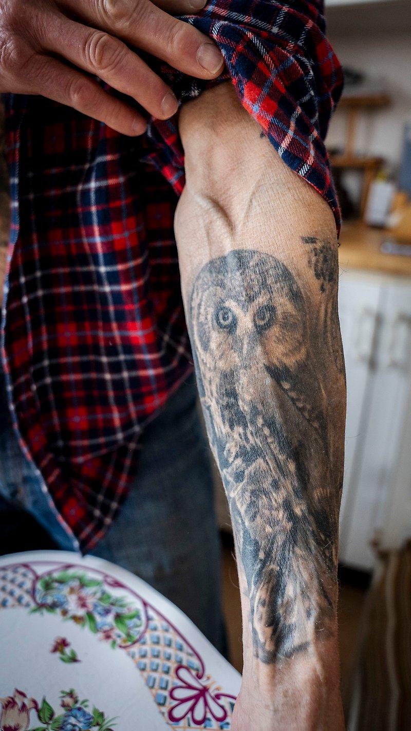 Albin kavlar upp sin skjortärm och visar en tatuering av en uggla som täcker hela hans underarm.