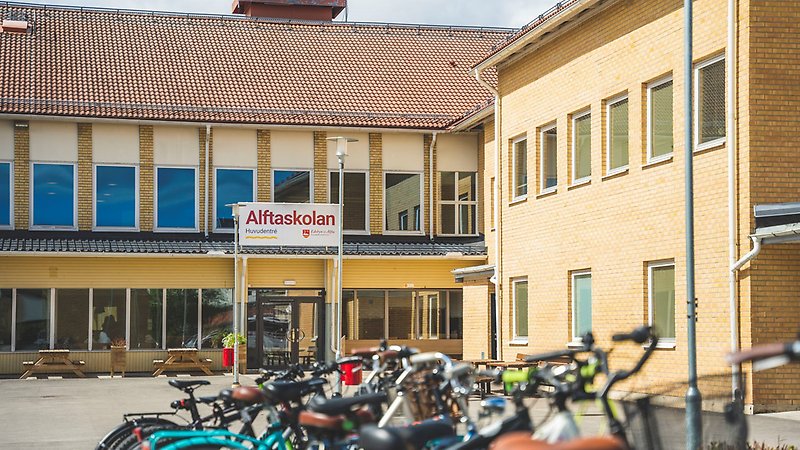 Huvudentré Alftaskolan i bakgrunden, parkerade cyklar på rad i förgrunden.