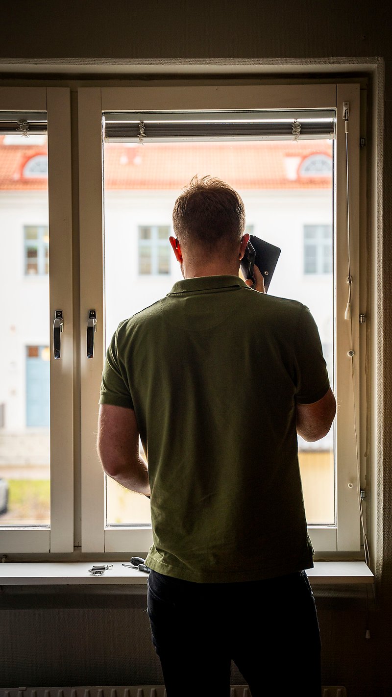 Christoffer Karlström står vid ett fönster och pratar i telefon.